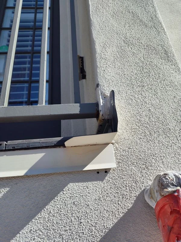 Metal railing attachment meeting a stucco wall beside a window