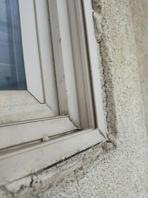 Close-up of separation and dark discoloration along a window frame and stucco joint